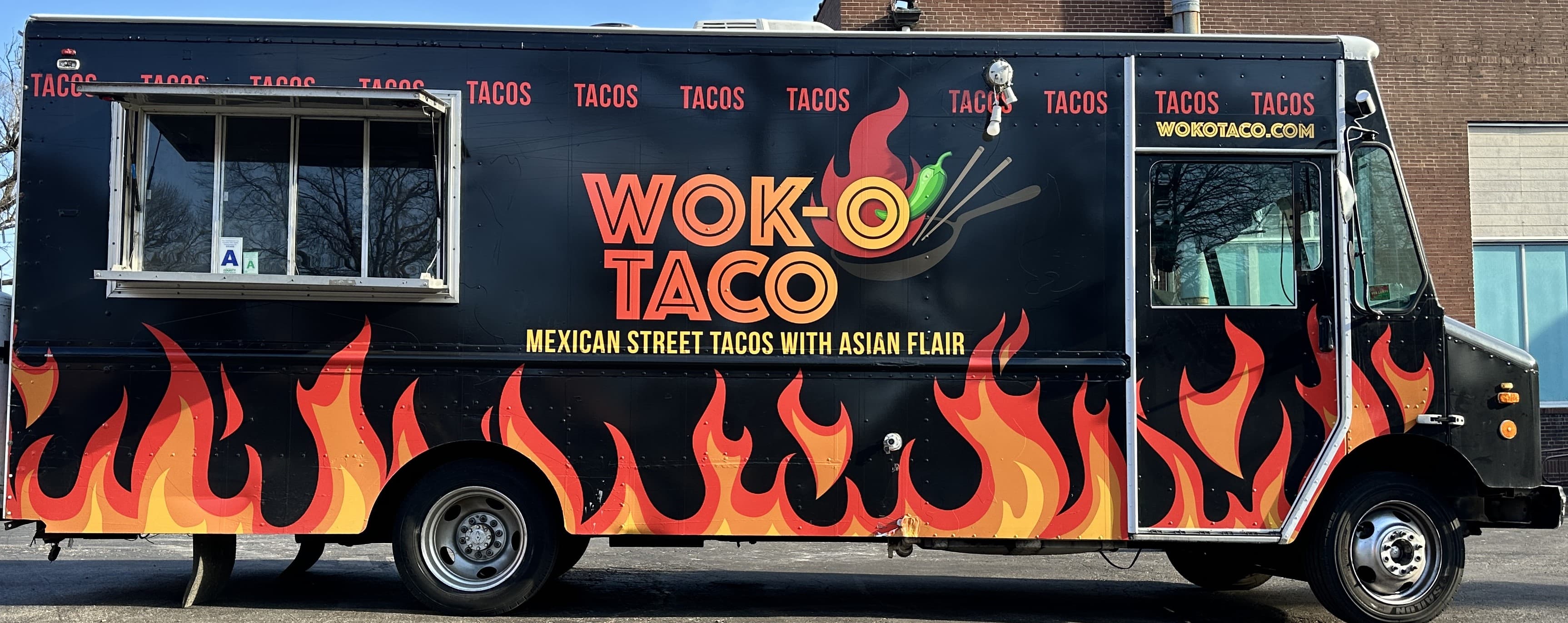 The Wok-O Taco truck in full side profile — black wrap with orange flame graphics and the service window open
