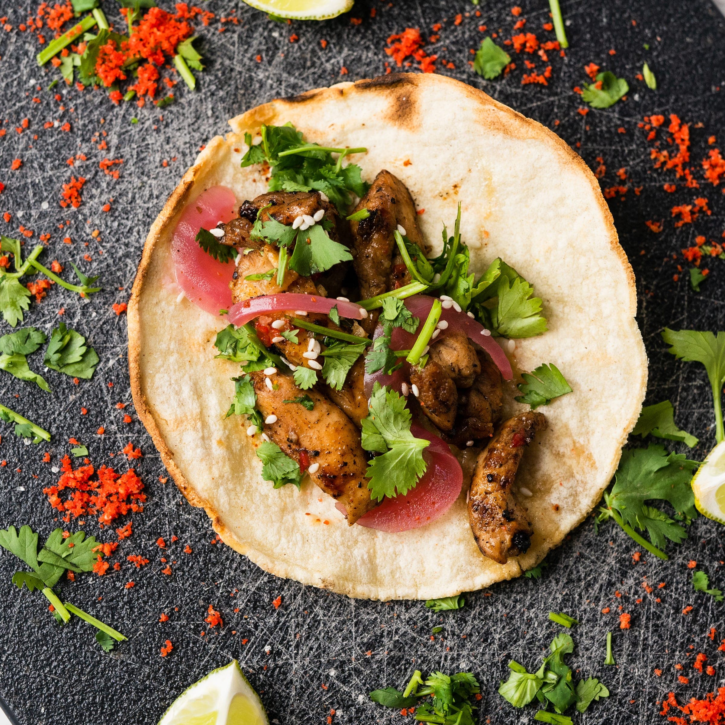 Overhead closeup of a chicken street taco on a charred tortilla with cilantro, pickled red onion, and sesame seeds