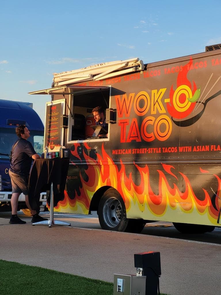 A guest at the food truck's service window under an awning as the evening sky dims