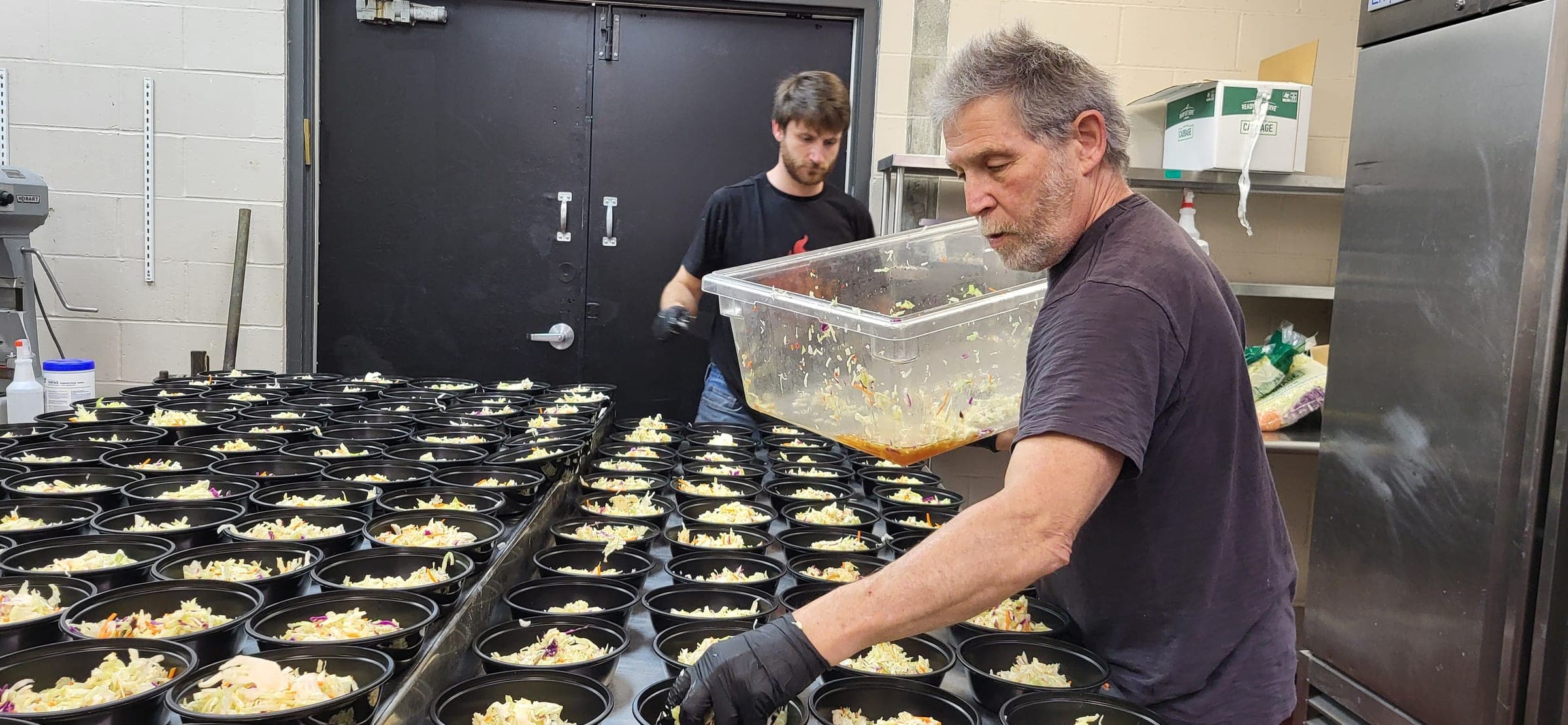 Two team members portioning individual bowls during catering prep in the kitchen