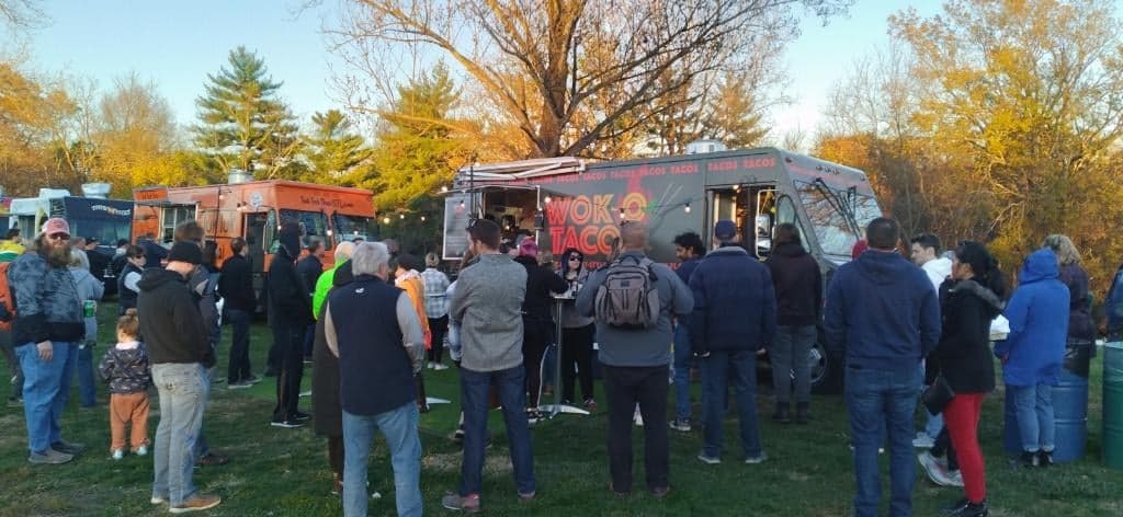 A line of guests at the Wok-O Taco service window at an outdoor event at dusk