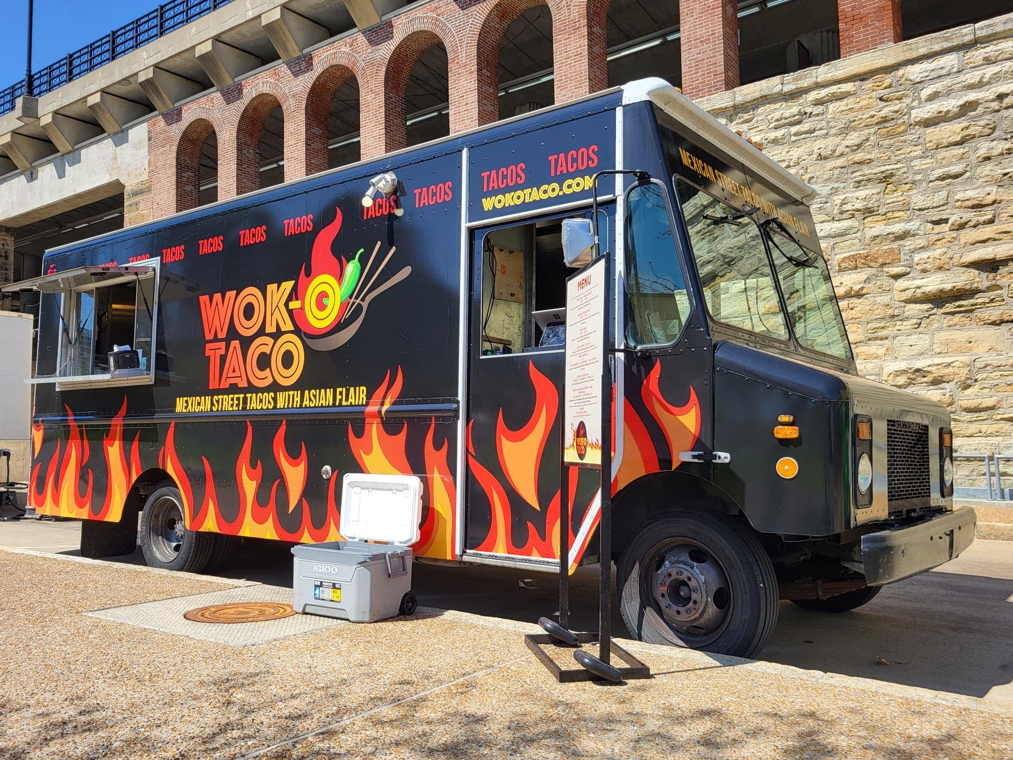The Wok-O Taco truck with its service window open, parked beside a stone arcade